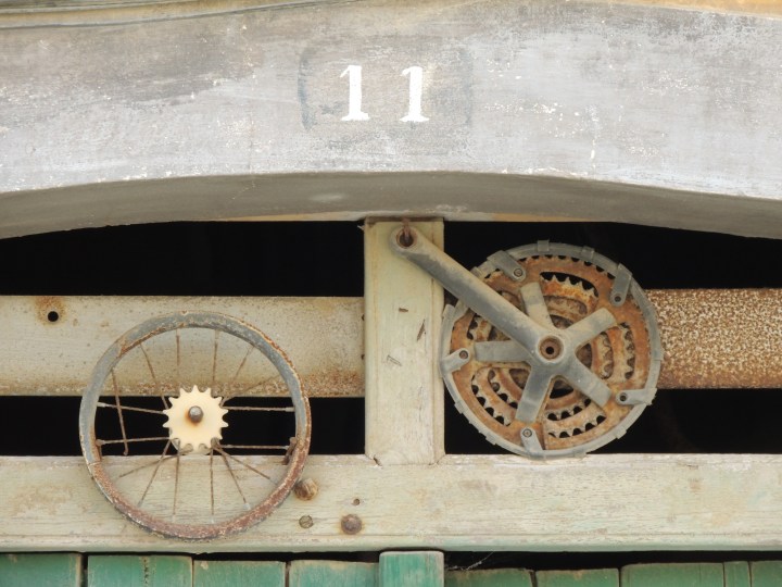 Close up above a door, with the number of 11 and two round shapes below. One looks like a bike wheel, the other a cog
