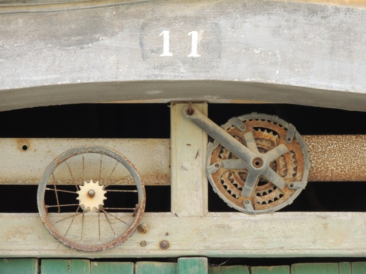 Close up above a door, with the number of 11 and two round shapes below. One looks like a bike wheel, the other a cog